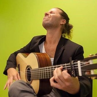 Färgfoto av en man som sitter och spelar gitarr inlevelsefullt med en limegrön bakgrund